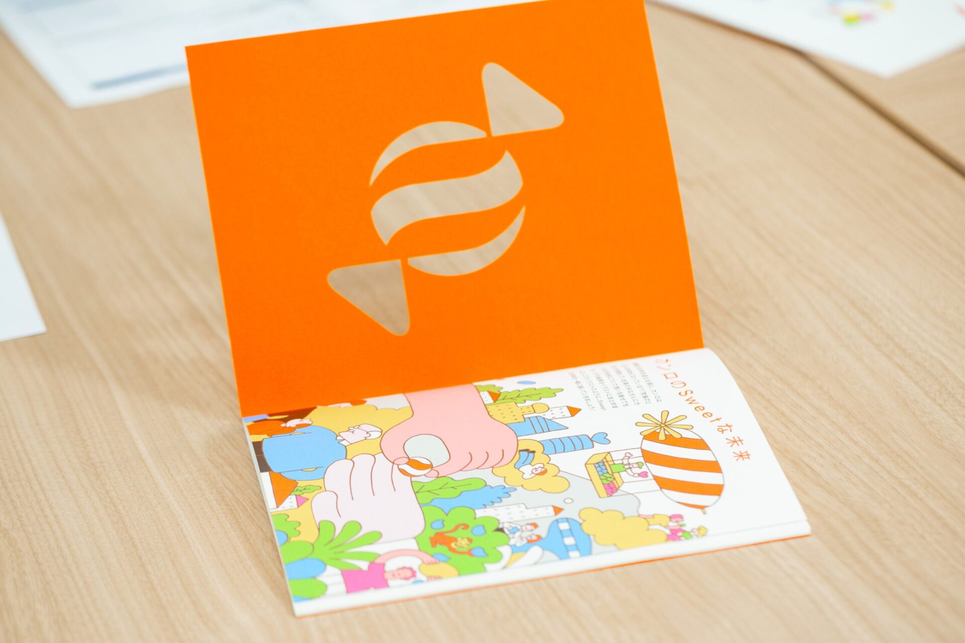 表紙を開けると、1ページ目に片観音折りで「カンロのSweetな未来」として、カンロの未来予想図のイラストが現れる。イラストはイラストレーターの市村譲氏によるもの。【撮影：栃久保誠】